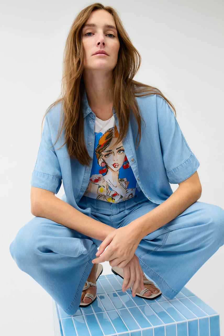 Casual T-shirt: Woman in graphic tee with blue denim jacket and pants, sitting confidently.