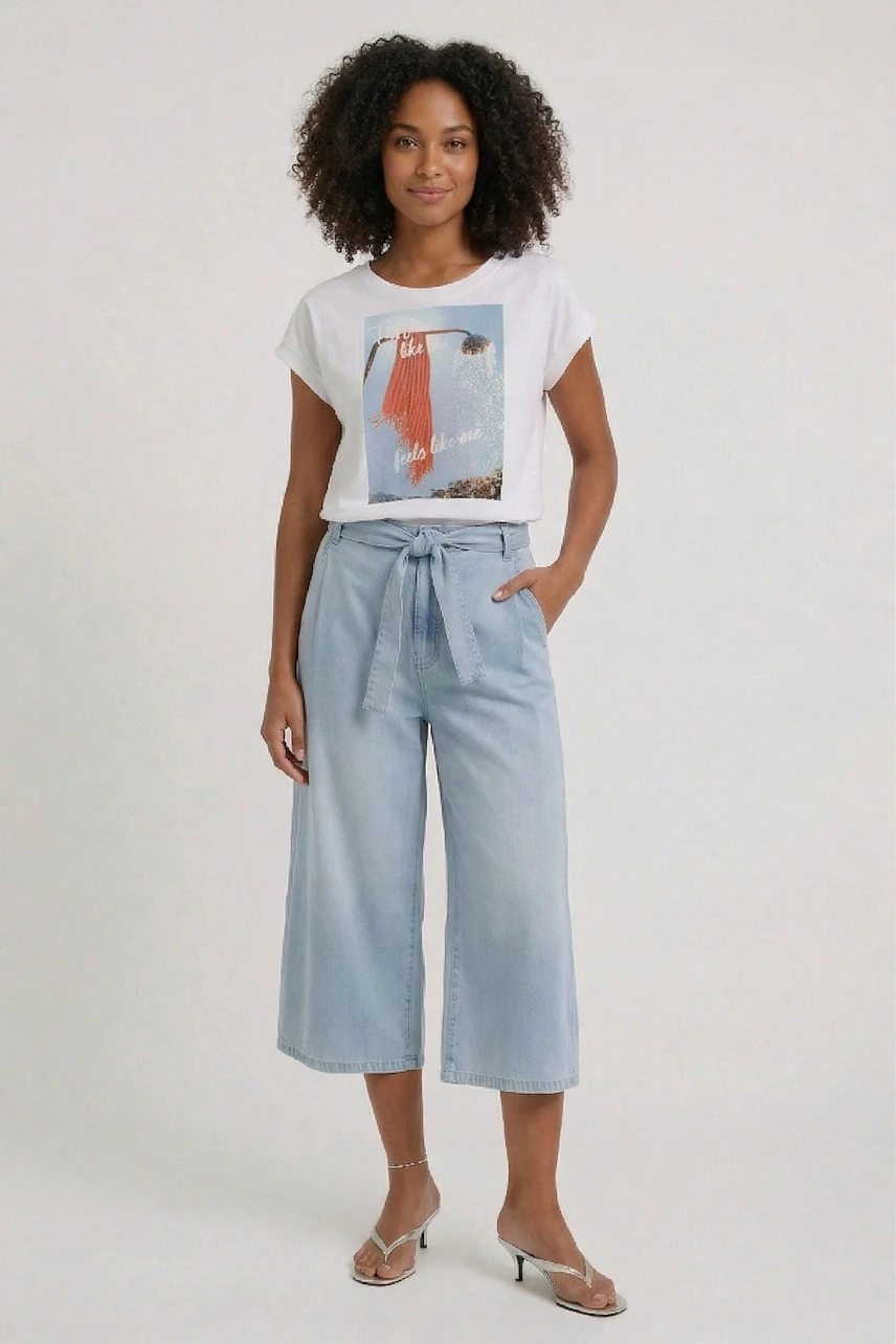 Casual T-shirt: Woman in a white graphic tee with light blue wide-leg pants, hands in pockets, smiling.