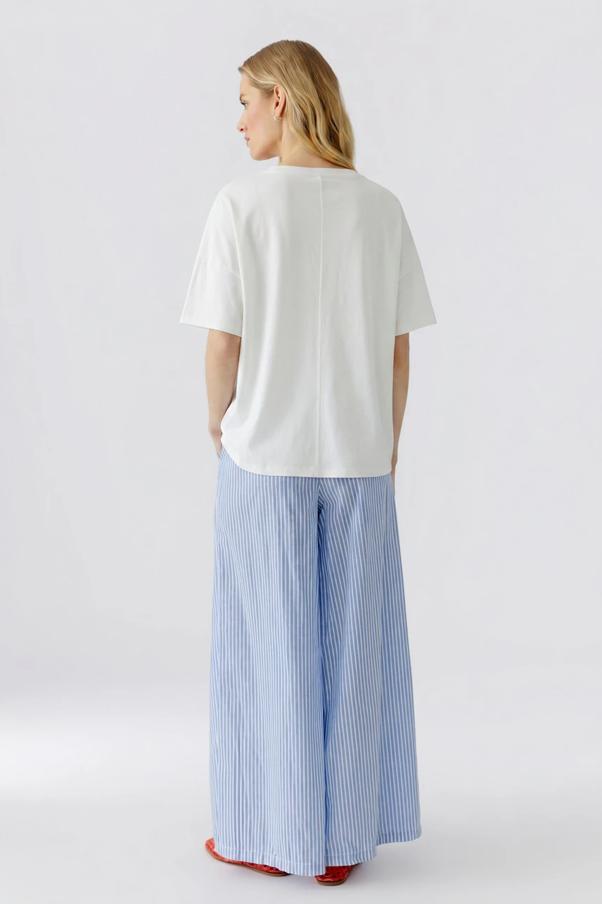 Weißes Damen-T-Shirt: Frau im locker sitzenden T-Shirt und hellen Jeans, von hinten gesehen.