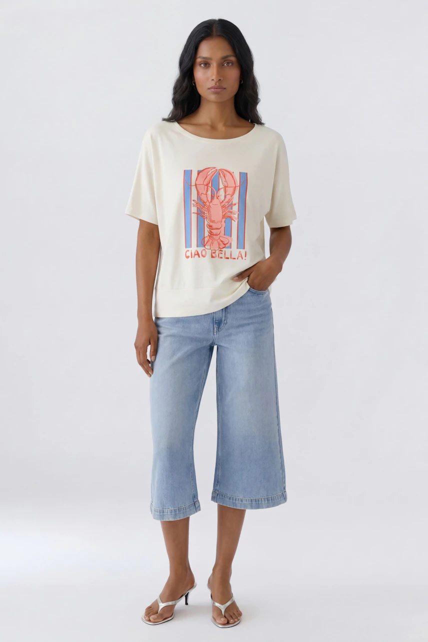 Casual women's T-shirt: Woman in graphic tee with lobster print and "Ciao Bella!" text, paired with denim culottes.