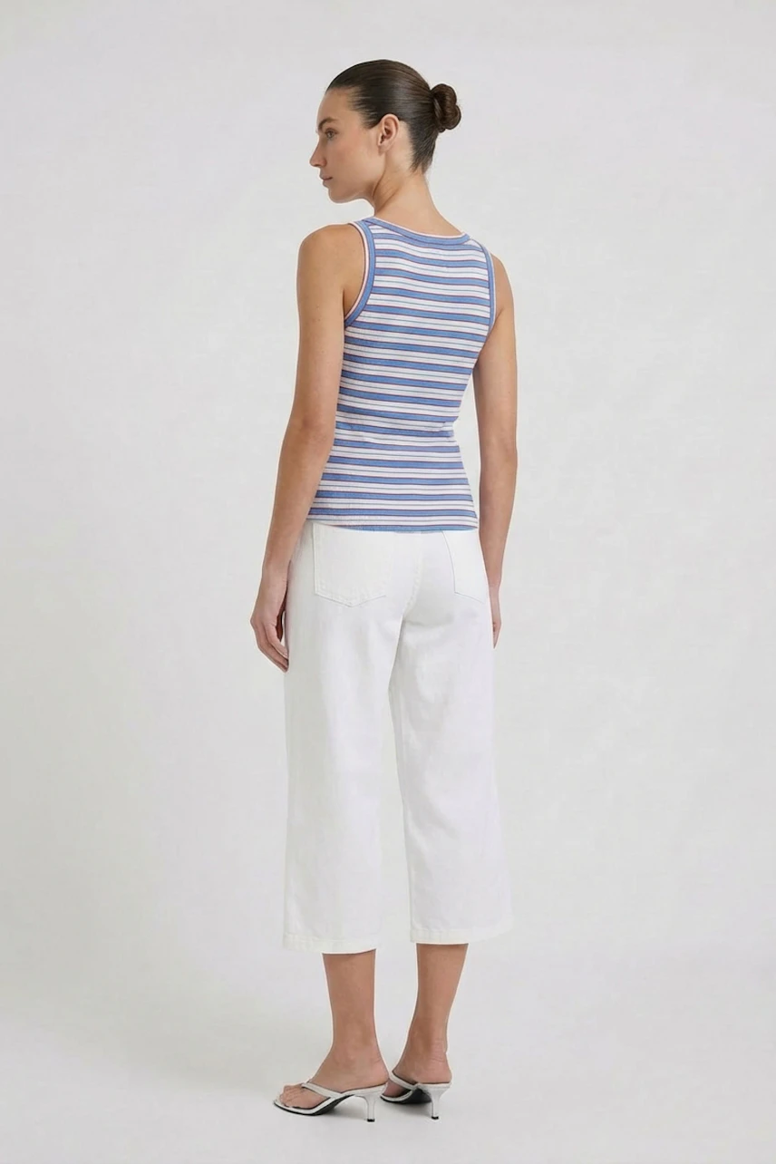 Striped tank top: Woman in blue and white striped tank top with white pants, standing confidently.