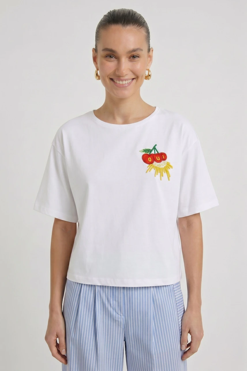 Casual women's T-shirt: Smiling woman in white T-shirt with colorful fruit embroidery, paired with striped pants.