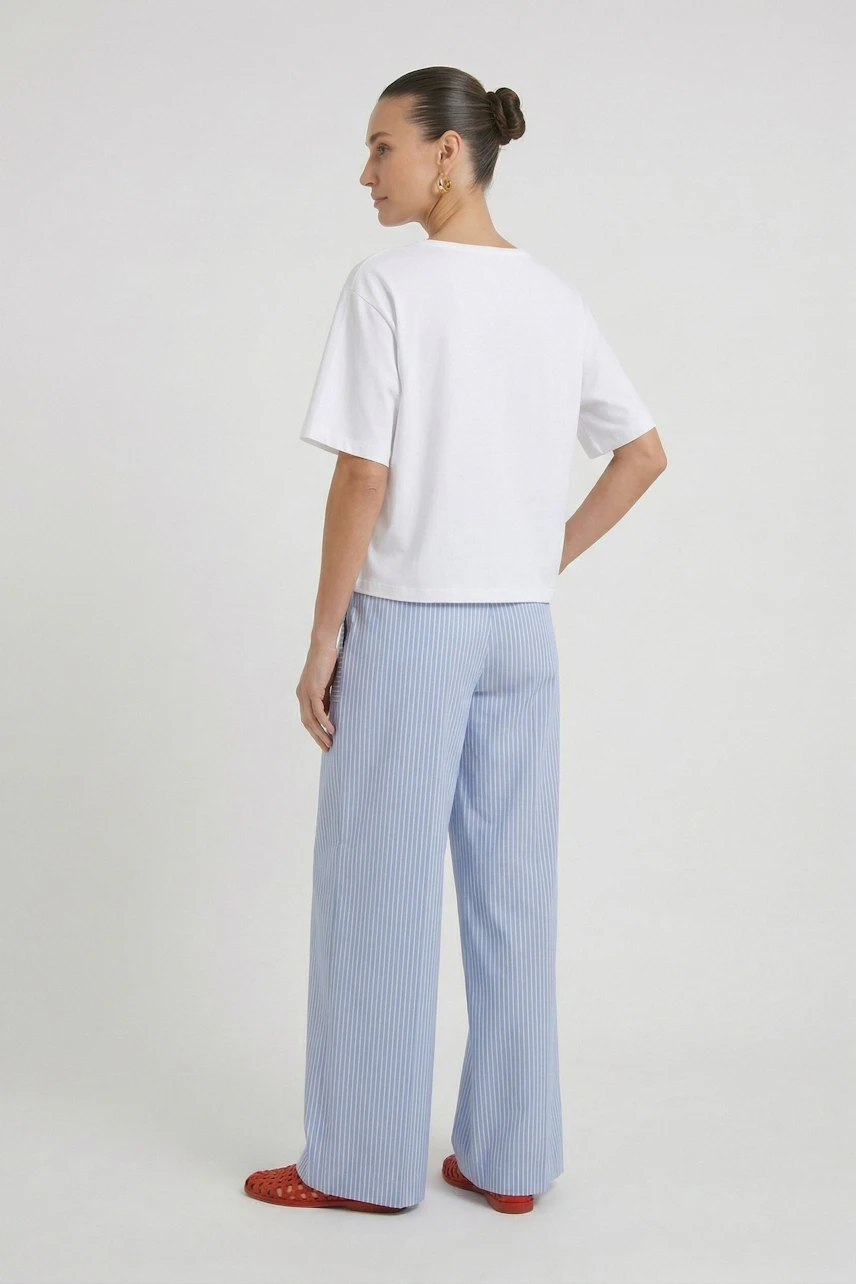 Casual T-shirt: Woman in a white T-shirt and striped pants, looking relaxed with hair in a bun.
