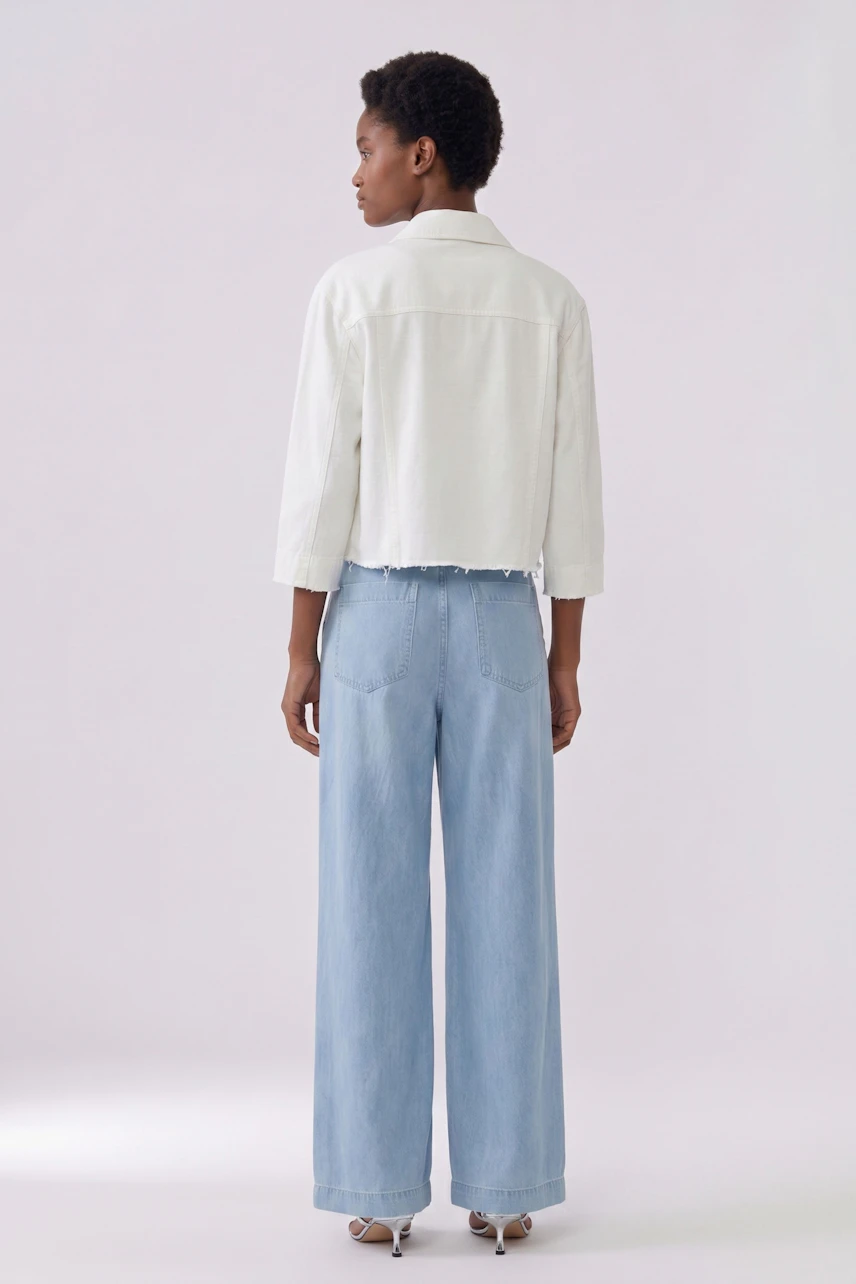 Casual denim jacket: Woman in a white cropped jeans jacket and light blue wide-leg jeans, standing confidently.