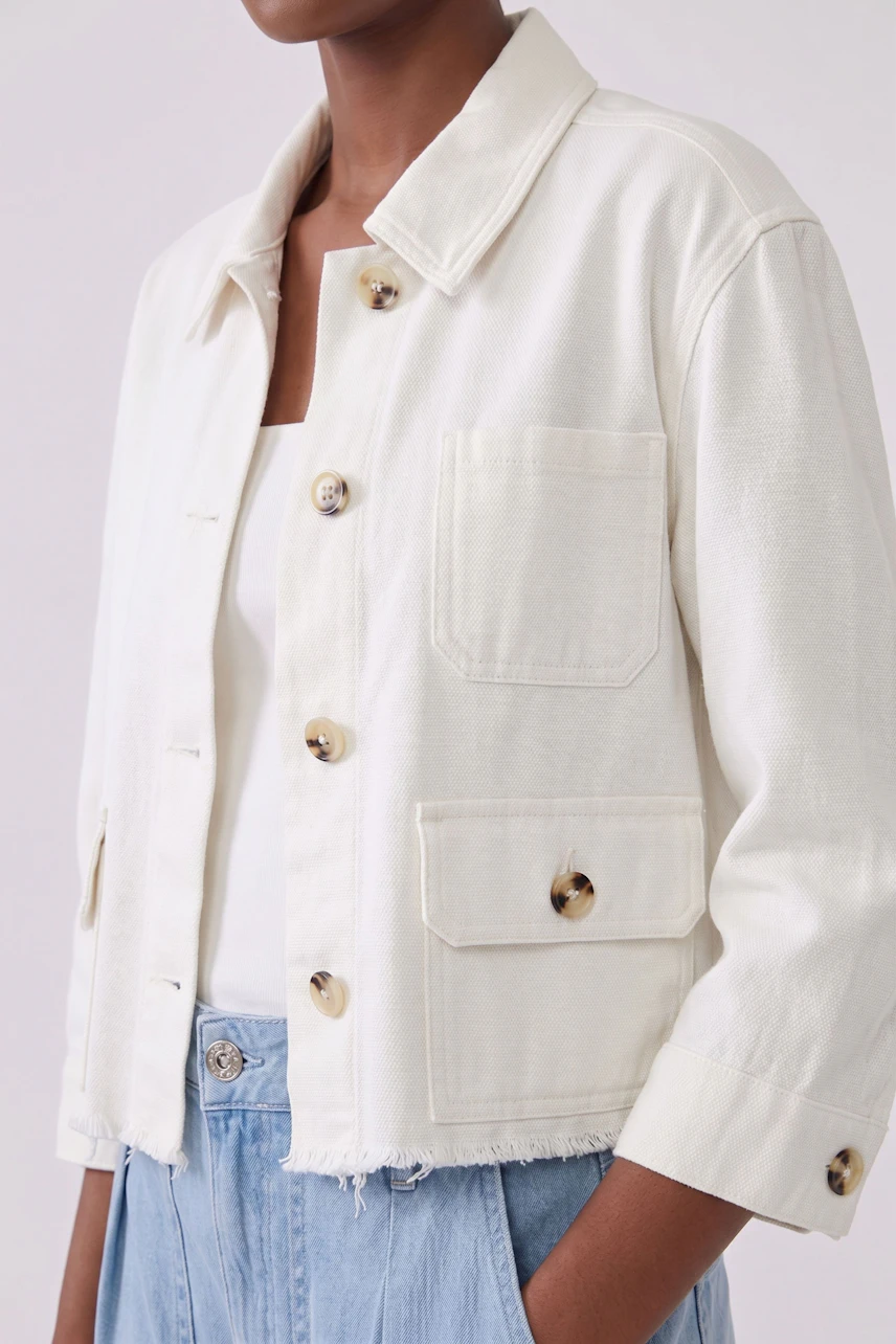 Casual women's denim jacket: Woman in a white denim jacket with large buttons and light blue jeans.
