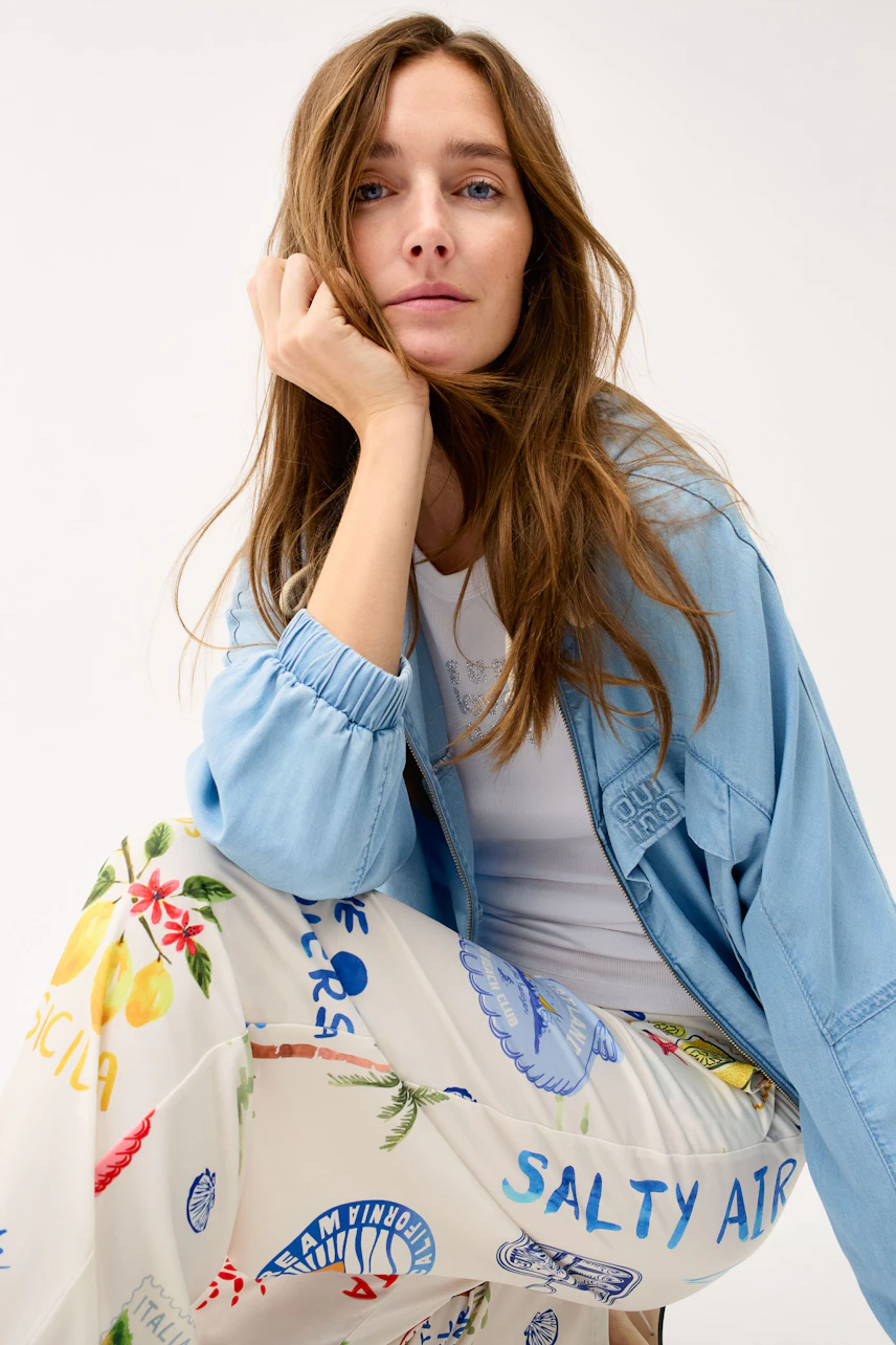 Casual women's jacket: Woman in light blue jacket with colorful print pants, relaxed and stylish.