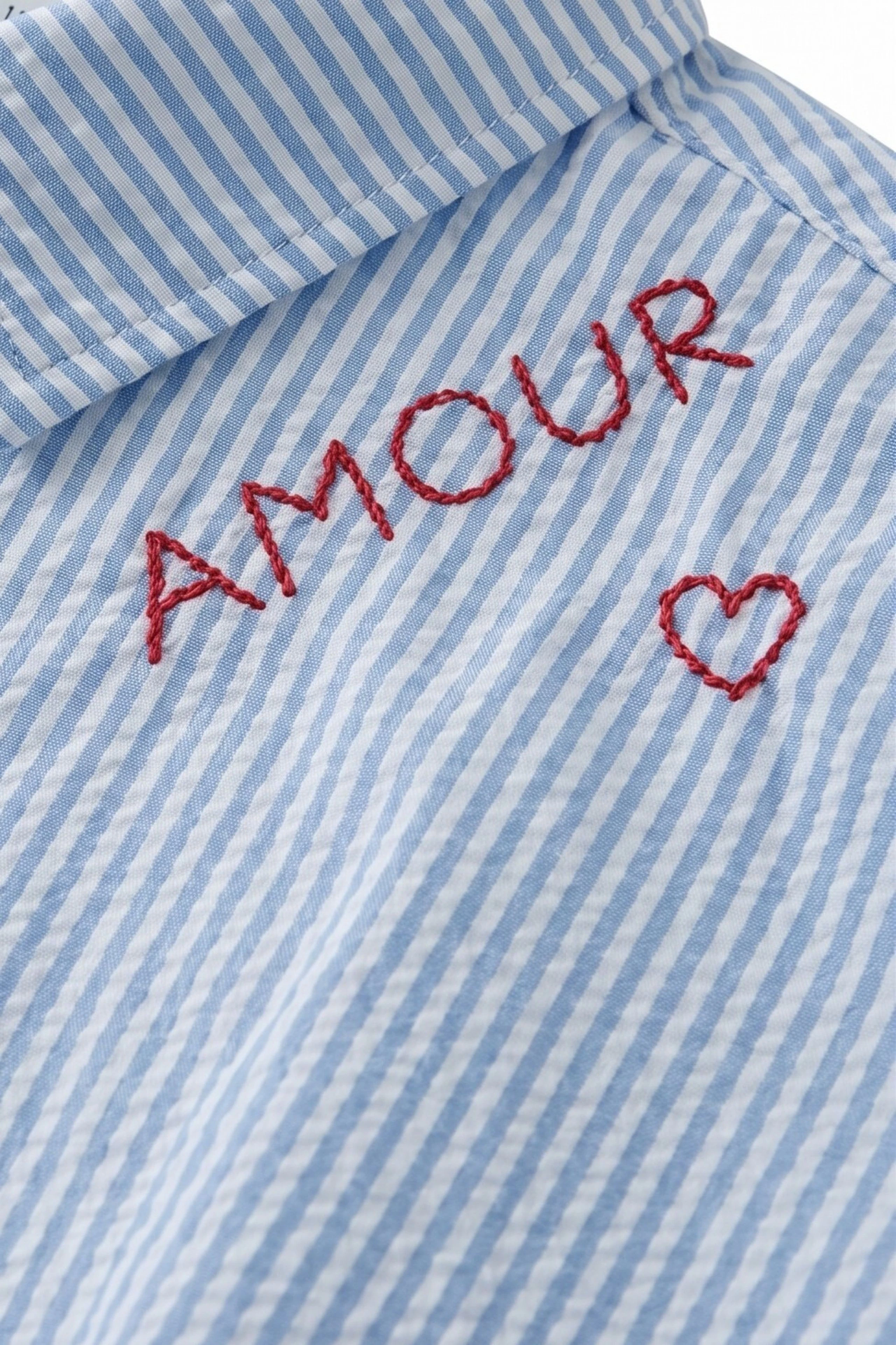 Gestreifte Bluse mit Stickerei: Blau-weiß gestreifte Bluse mit rotem Schriftzug "Amour" und Herzmotiv.