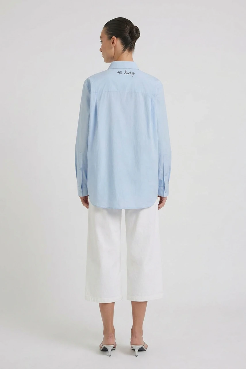 Casual women's blouse: Woman in light blue blouse with white wide-leg pants, standing confidently.