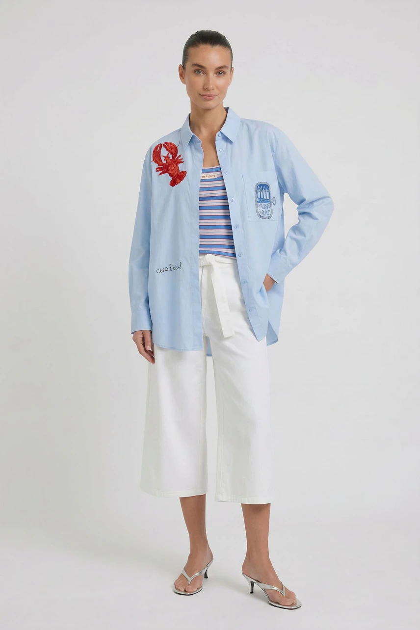Casual blouse: Woman in light blue blouse with red lobster print, striped top, and white culottes.