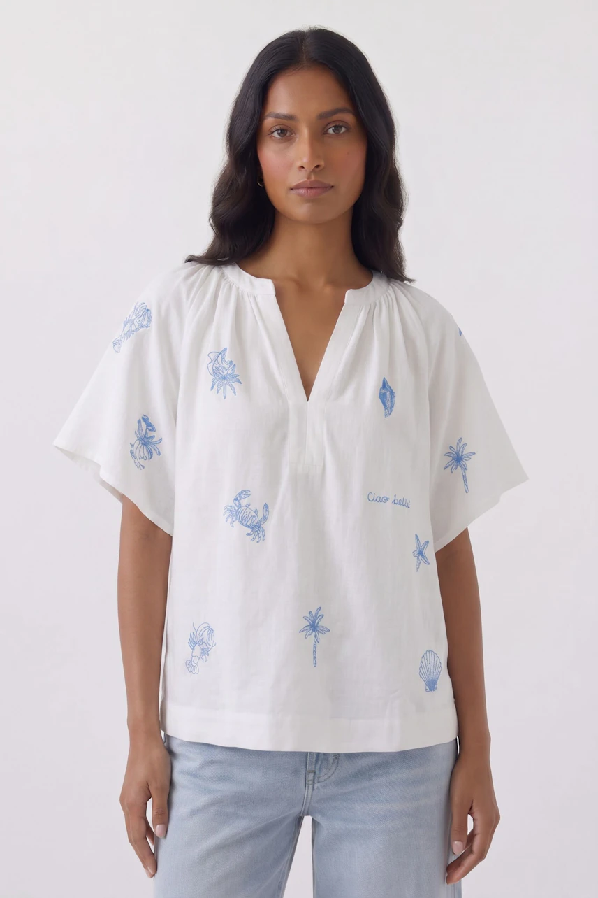 Casual blouse: Woman in white blouse with blue embroidery, short sleeves, and relaxed fit.