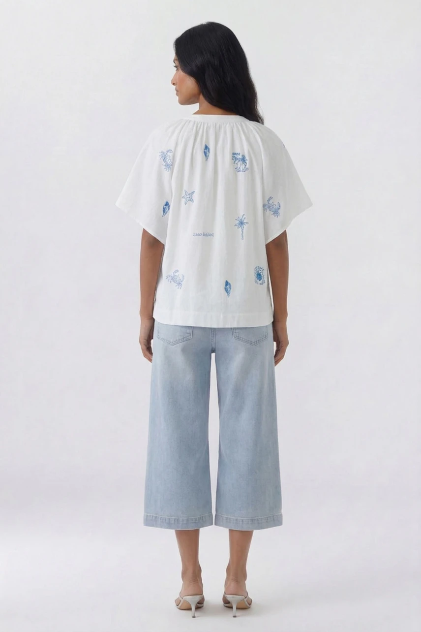 Casual blouse: Woman in white blouse with blue prints, paired with light denim culottes, facing away.