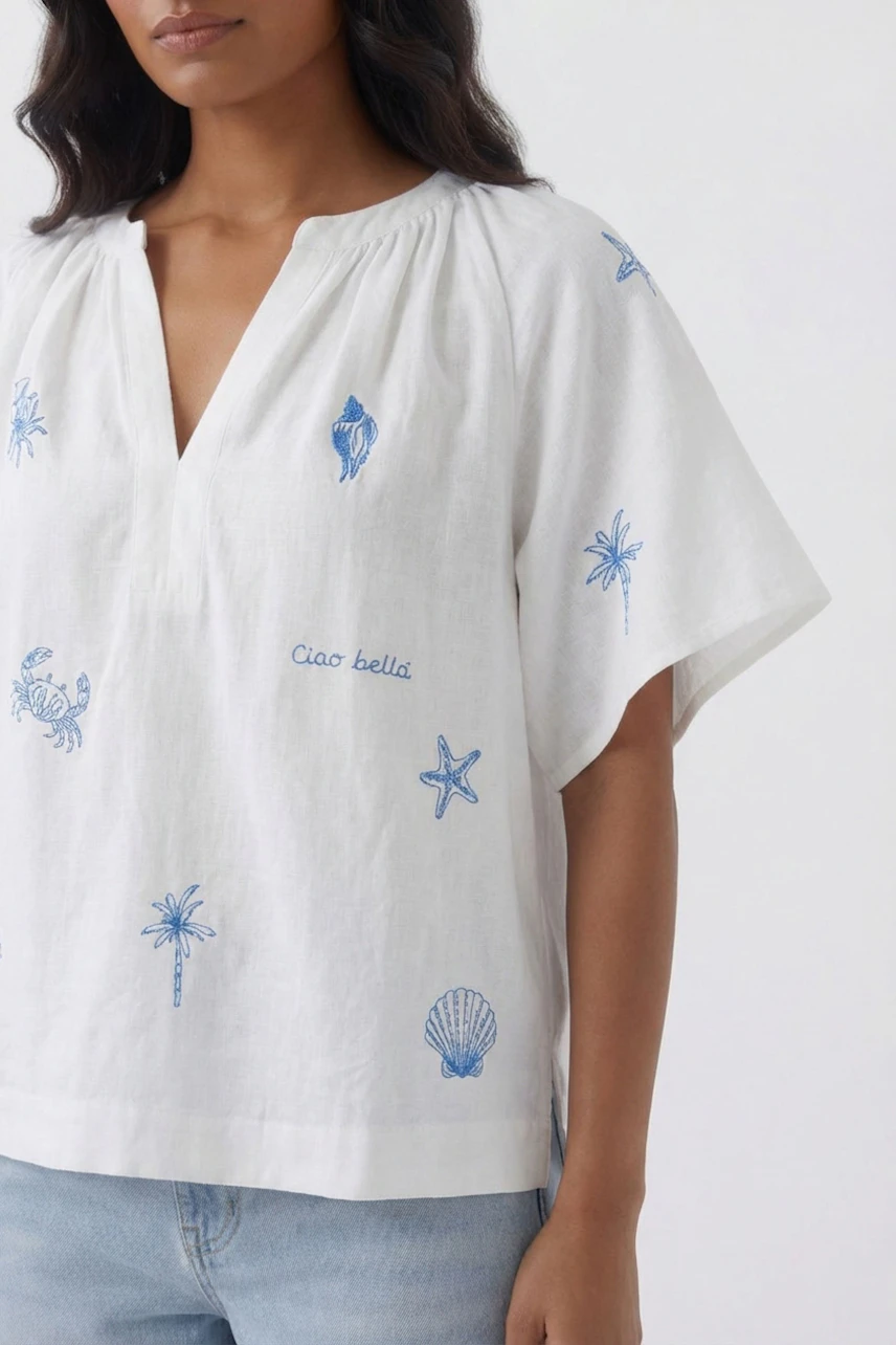 Casual blouse: Woman in white blouse with blue embroidery, short sleeves, and relaxed fit.