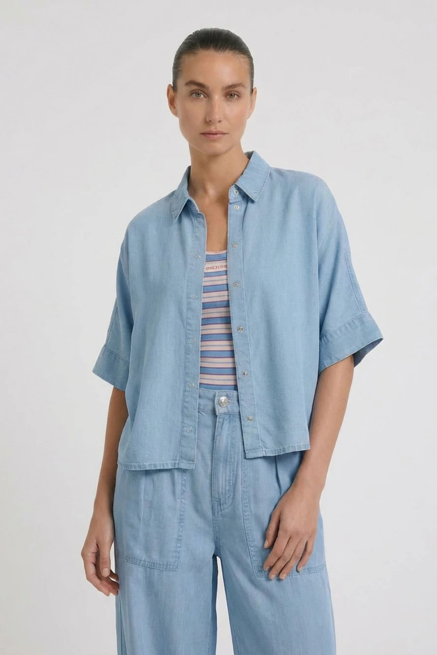 Casual women's blouse: Woman in light blue denim blouse over striped top, paired with matching denim pants.