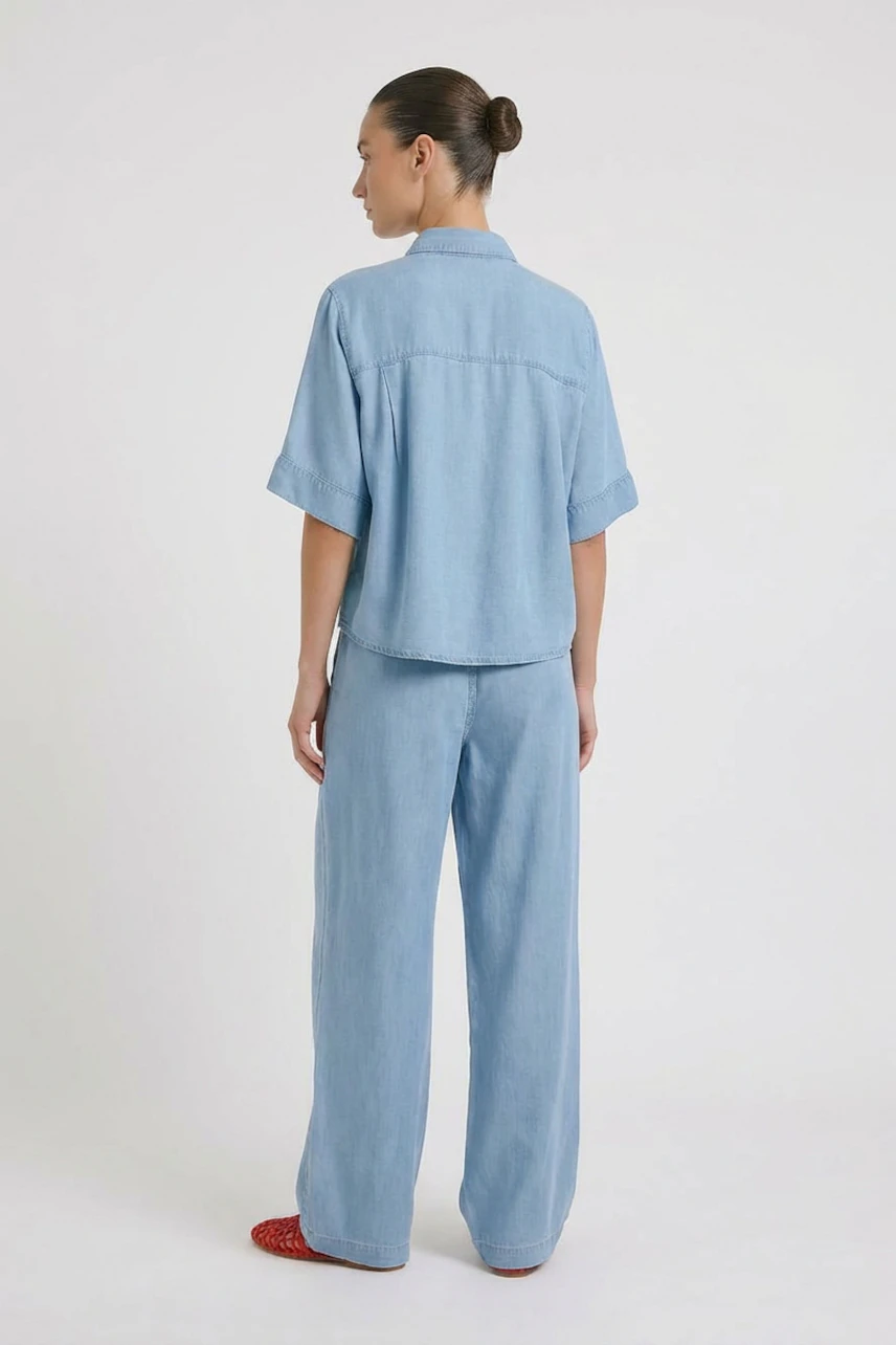 Casual women's blouse: Woman in light blue denim blouse with short sleeves, paired with matching wide-leg pants.