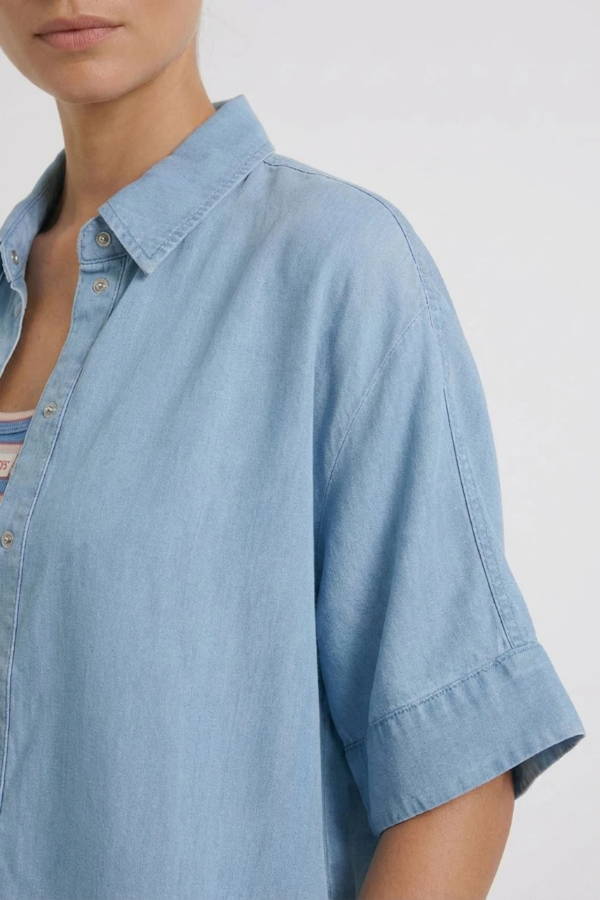Casual women's blouse: Woman in light blue denim blouse with short sleeves and a relaxed fit.