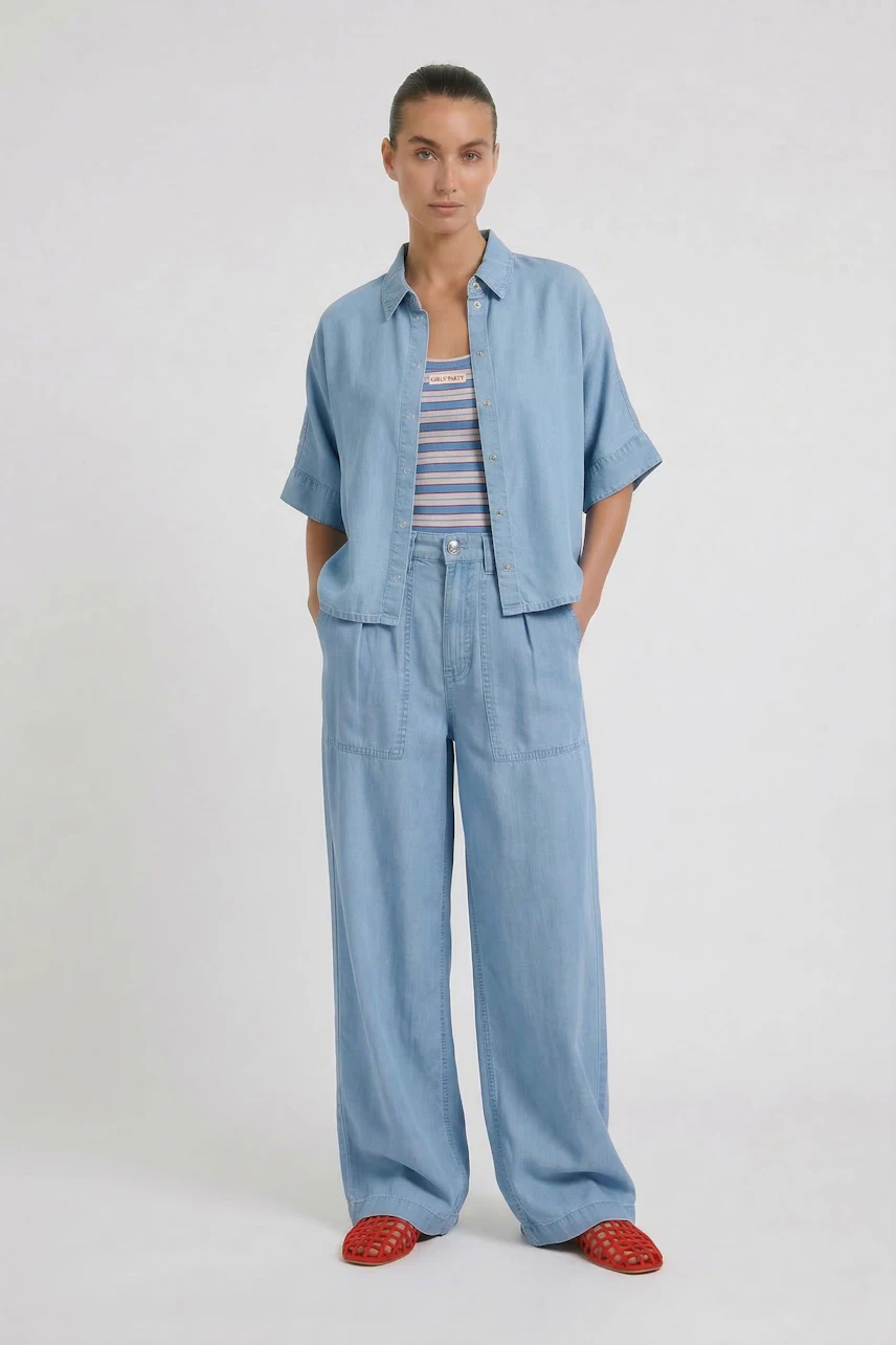 Casual blouse: Woman in light blue blouse and matching wide-leg pants, hands in pockets, relaxed look.