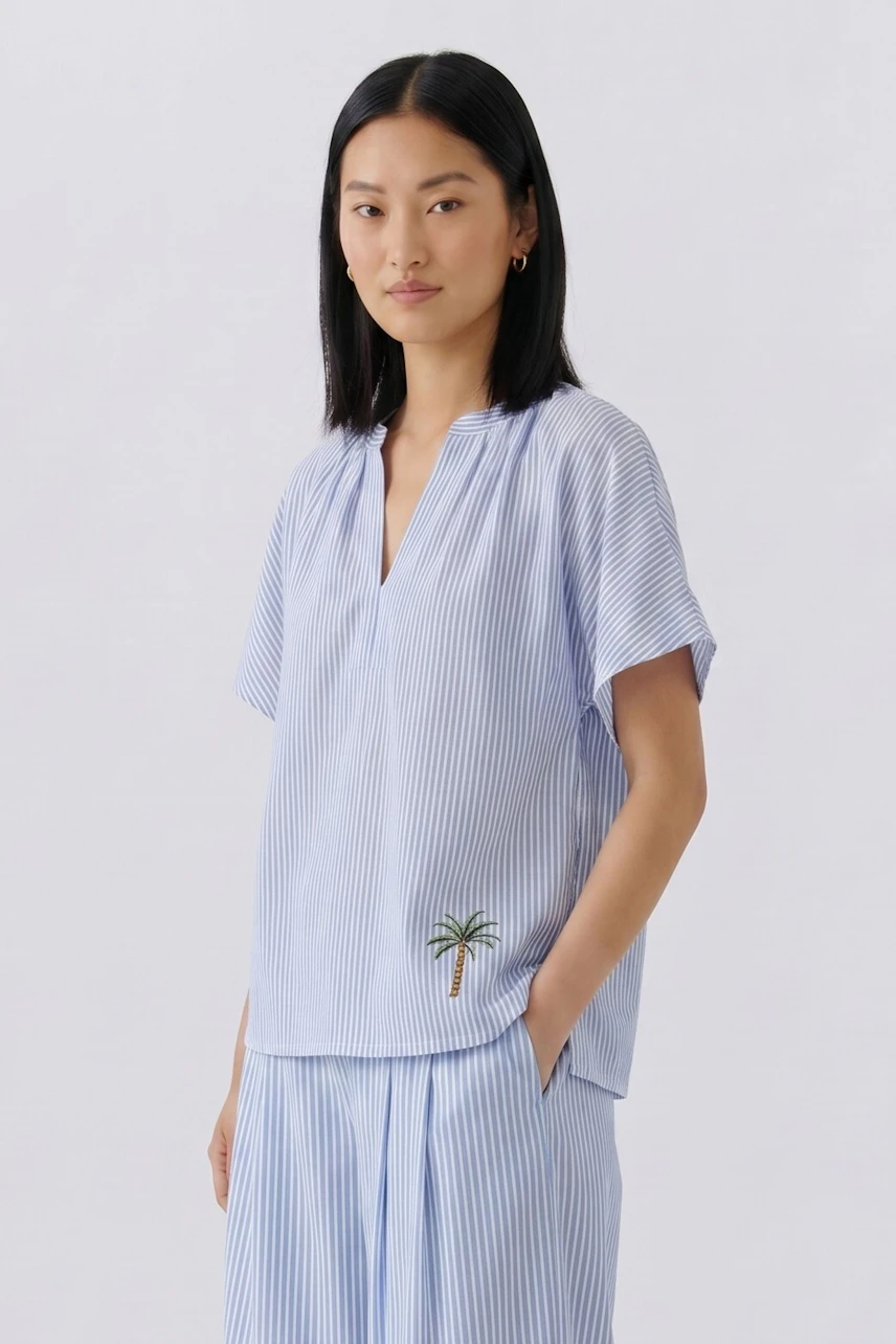 Casual blouse: Woman in a blue striped blouse with short sleeves and a palm tree detail, looking poised.
