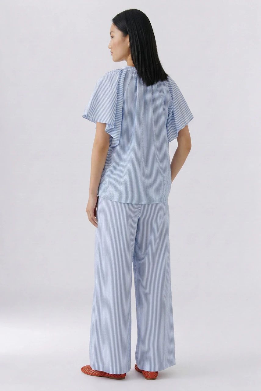 Casual blouse: Woman in light blue blouse with wide sleeves, paired with matching striped pants, facing away.
