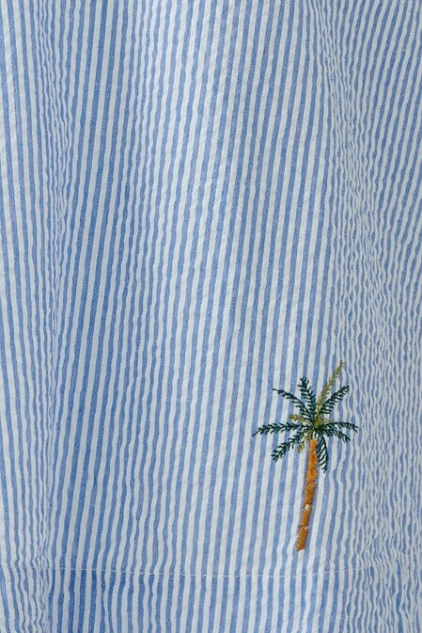 Casual women's blouse: Woman in a blue striped blouse with palm tree embroidery, relaxed fit.