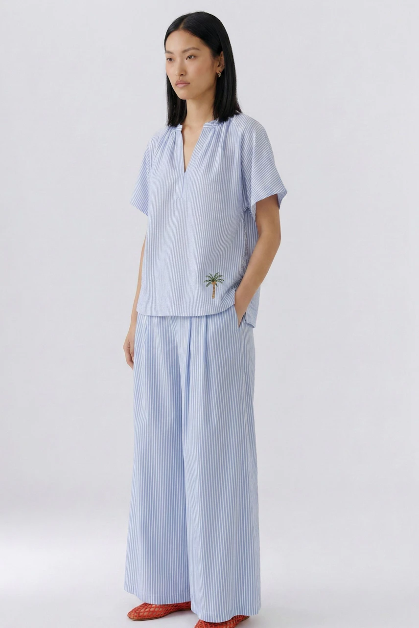 Casual blouse: Woman in a light blue striped blouse with short sleeves and a palm tree detail.