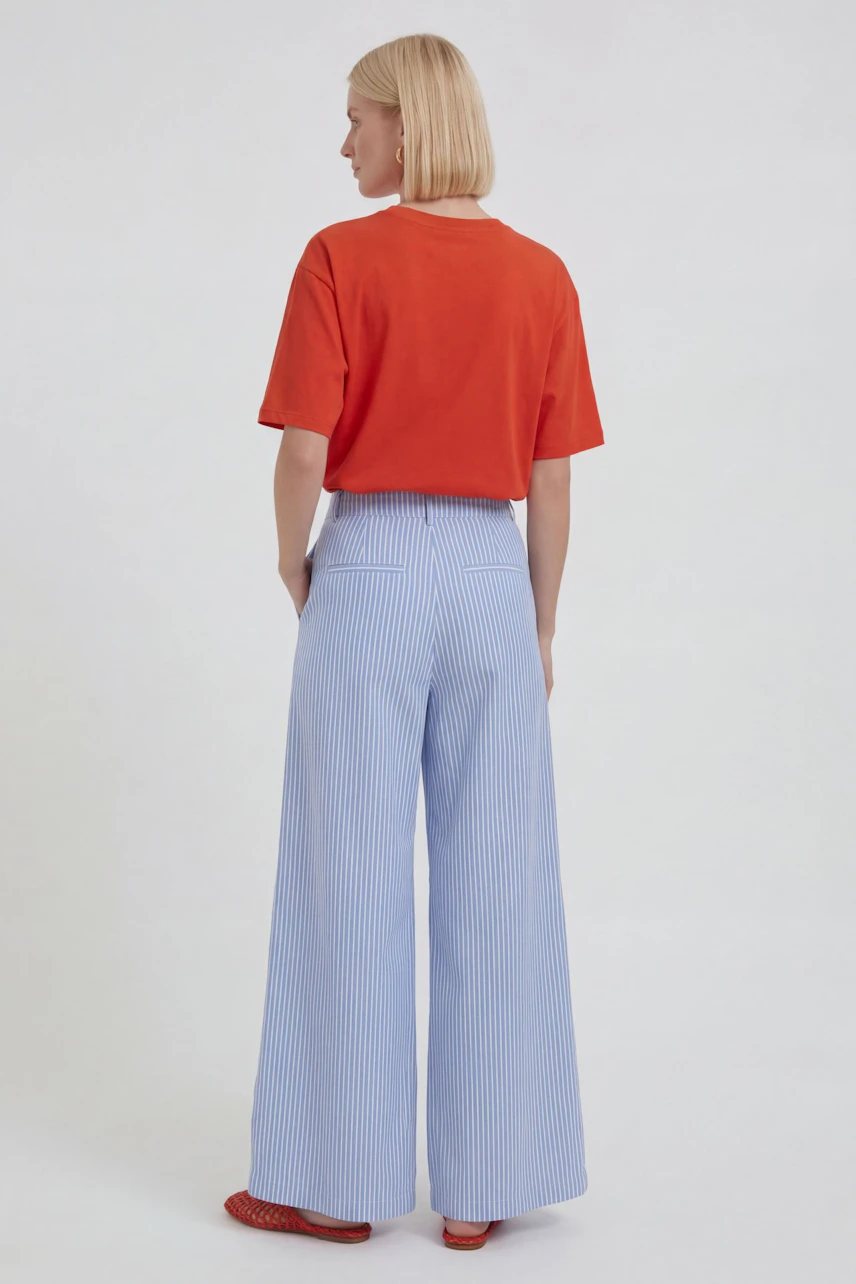 Woman in striped Marlene pants and red top, viewed from behind, showcasing relaxed fit and style.