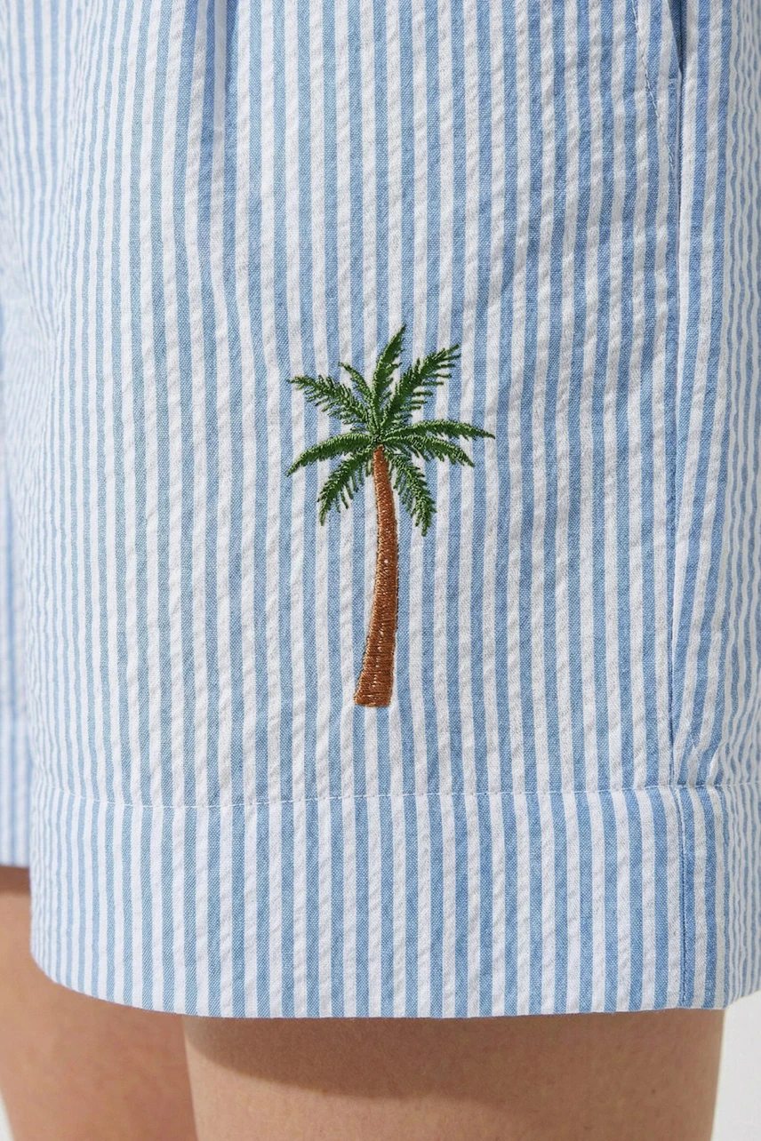 Striped shorts with palm tree embroidery, worn by a woman. Casual and stylish for summer days.
