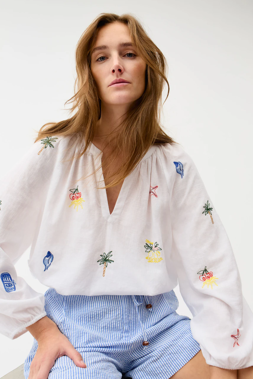 Casual shorts: Woman in blue striped shorts with a relaxed white blouse featuring colorful embroidery.