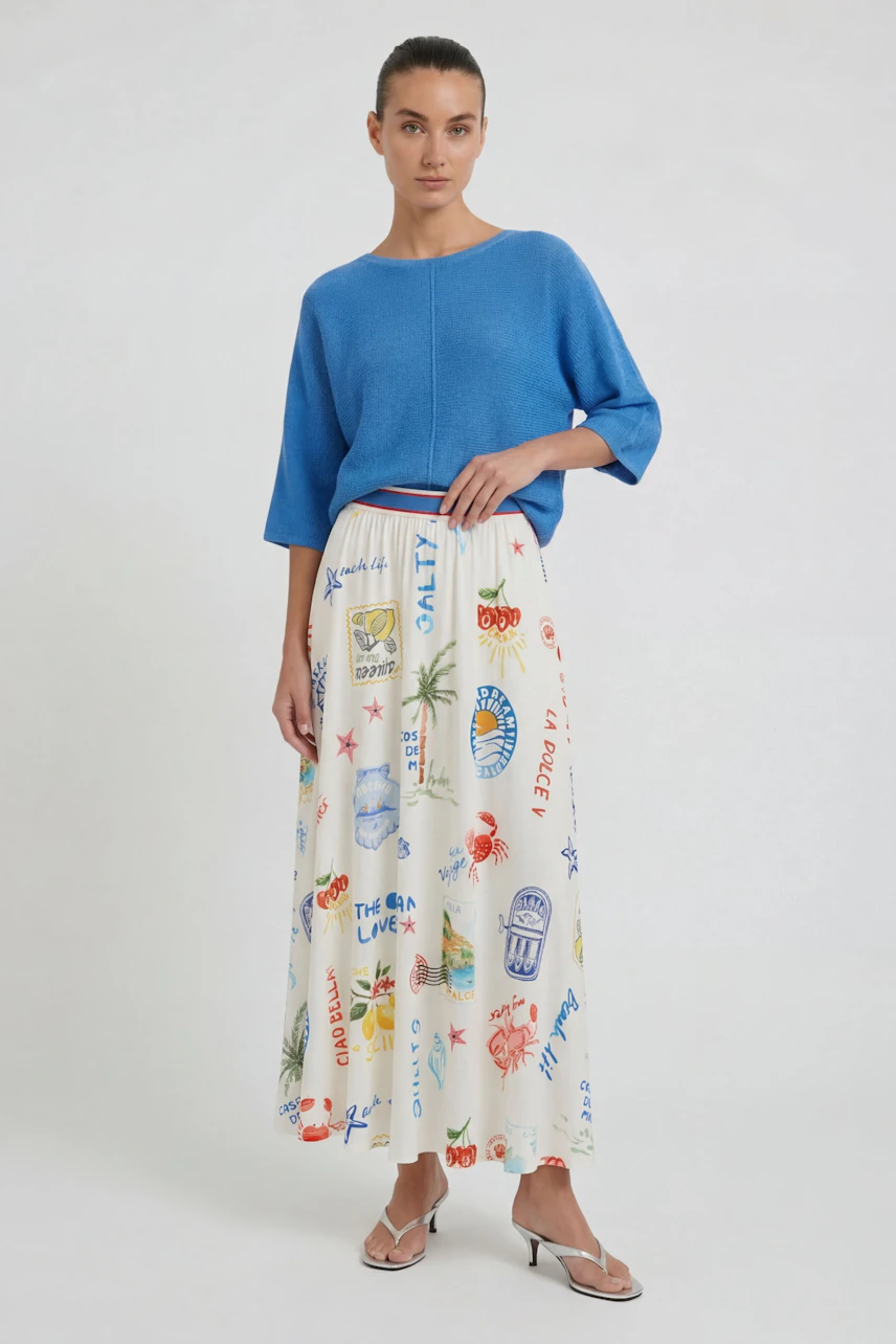 Woman in a vibrant maxiskirt with playful prints, paired with a blue top, standing confidently.