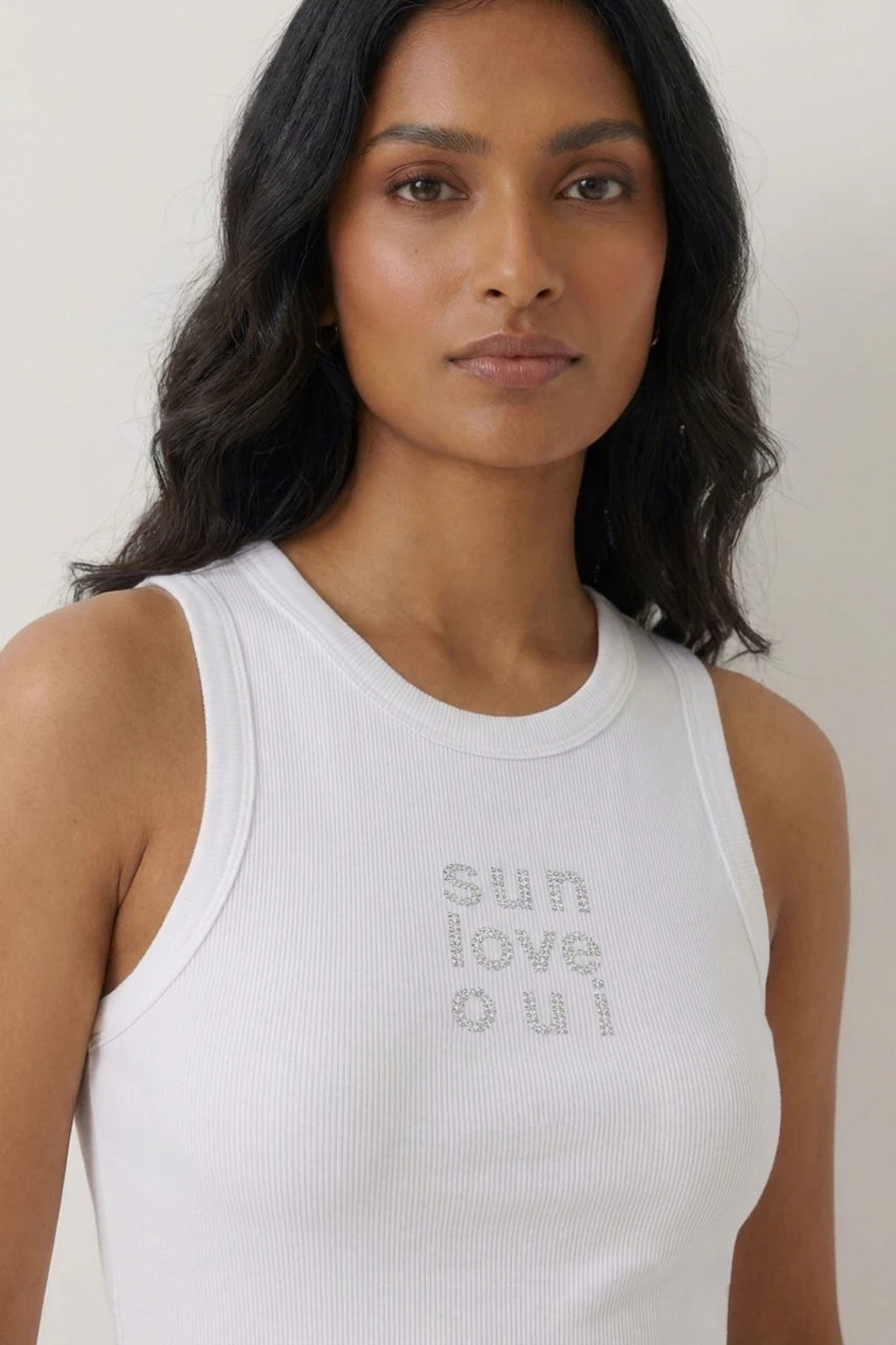 Woman in white tank top with 'sun love oui' text, casual and stylish look.