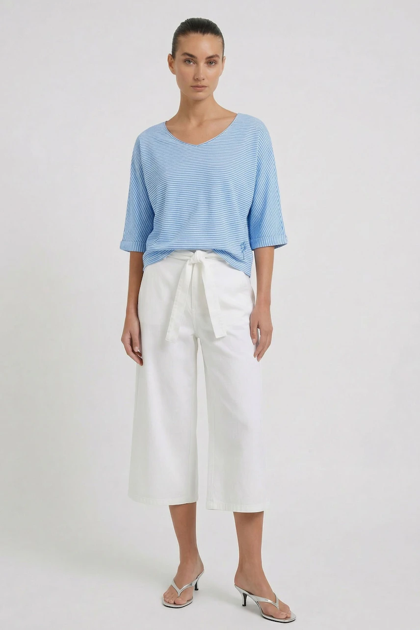 Casual women's T-shirt: Woman in a light blue T-shirt and white pants, standing confidently.