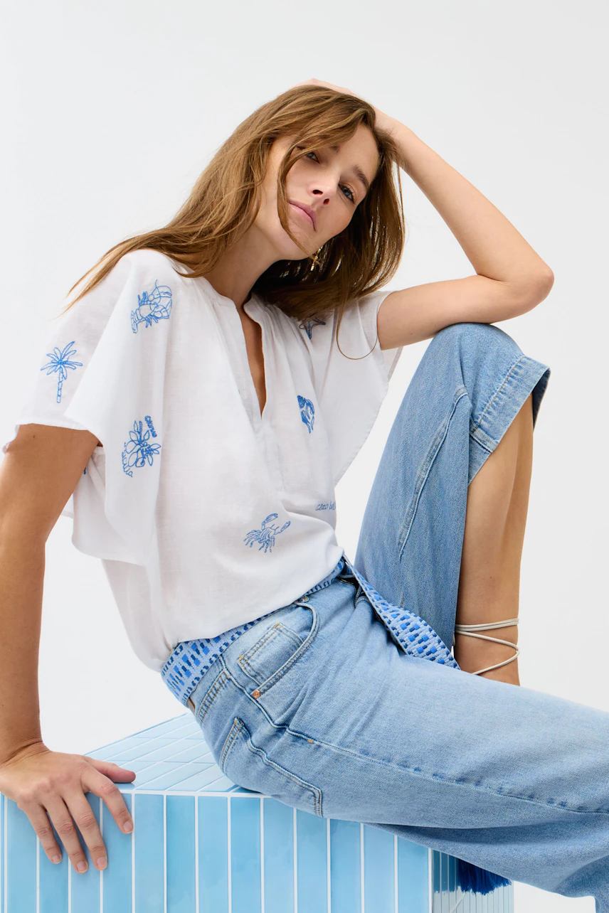 Casual culotte: Woman in light blue denim culotte with a relaxed white blouse, sitting confidently.