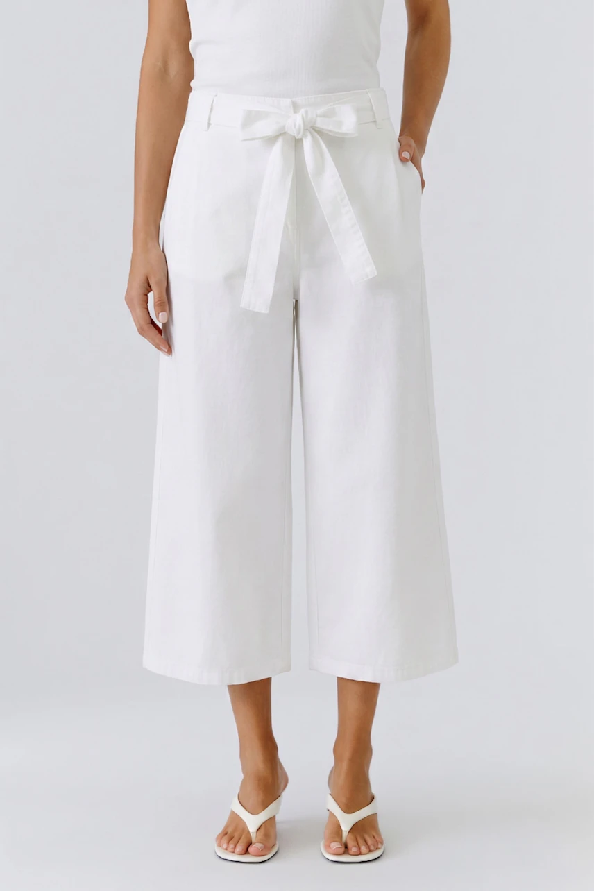 Woman in white culotte pants with a tied waist, paired with a simple top and sandals.