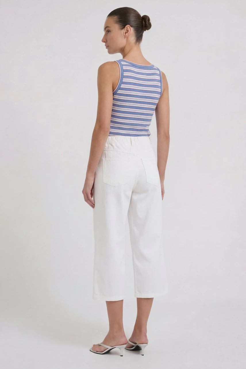 Woman in white culotte pants and striped tank top, side view. Casual and comfortable style.