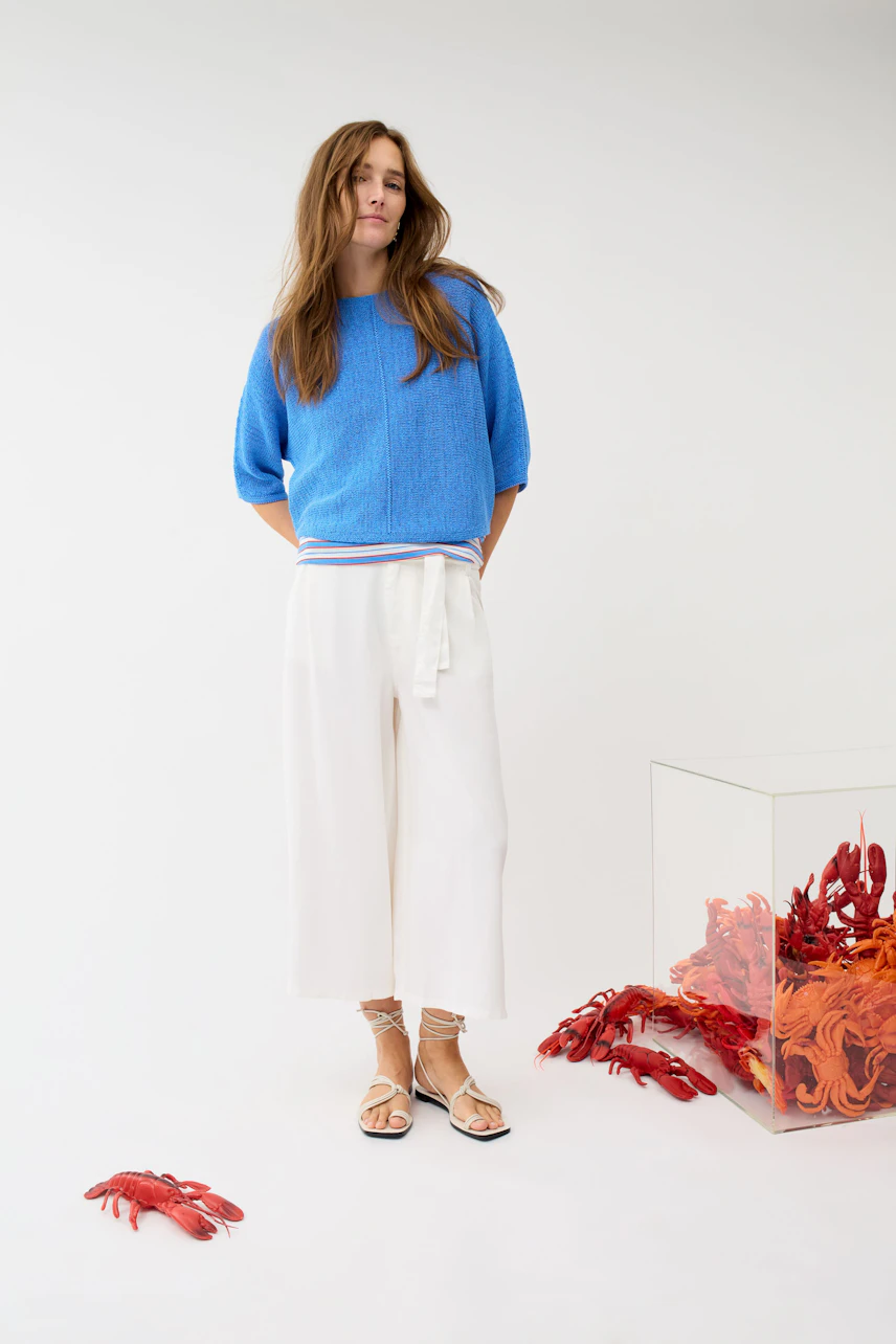 Woman in white culotte and blue pullover, standing confidently. Casual and stylish look.