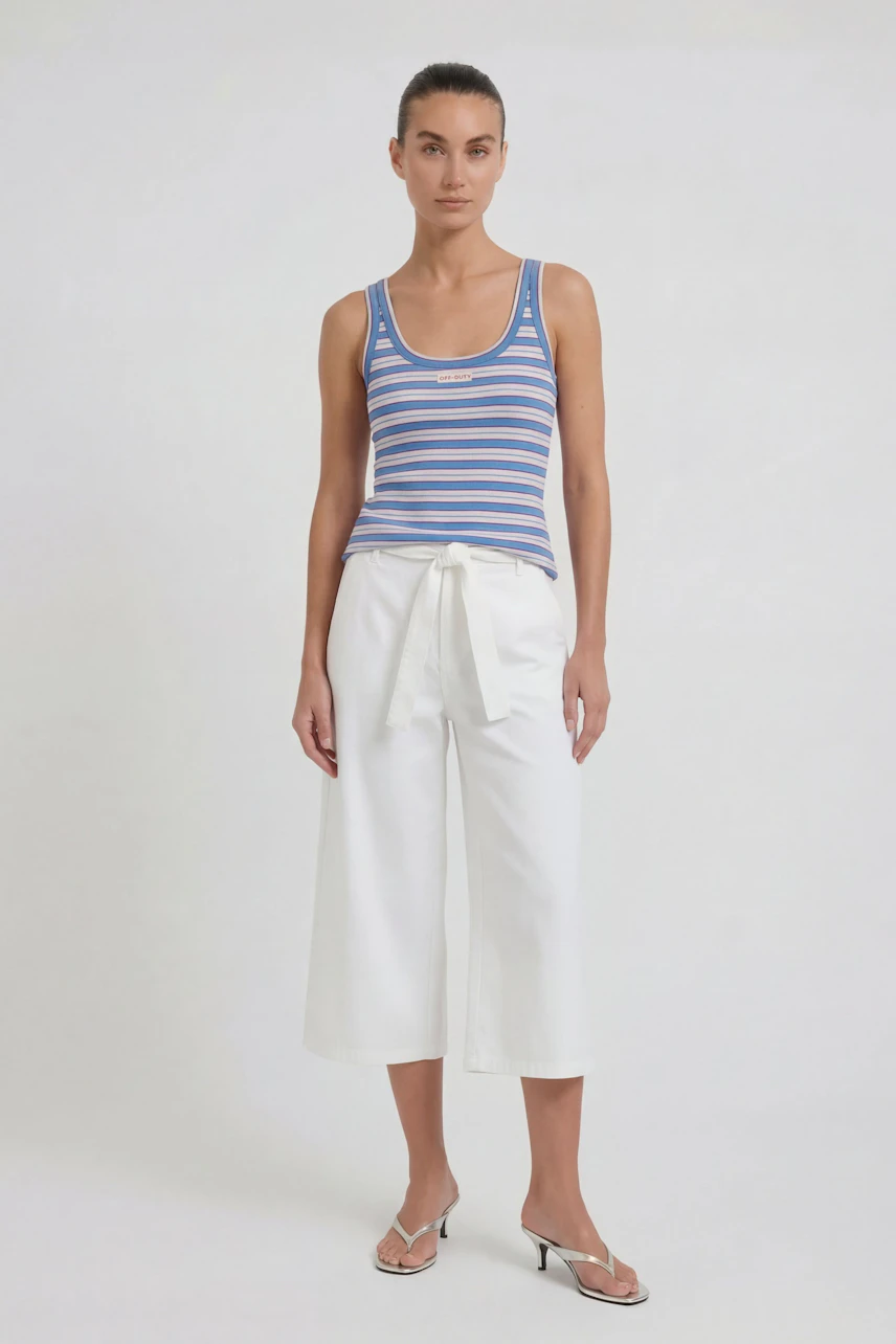 Woman in white culotte pants and striped tank top, standing confidently in sandals.