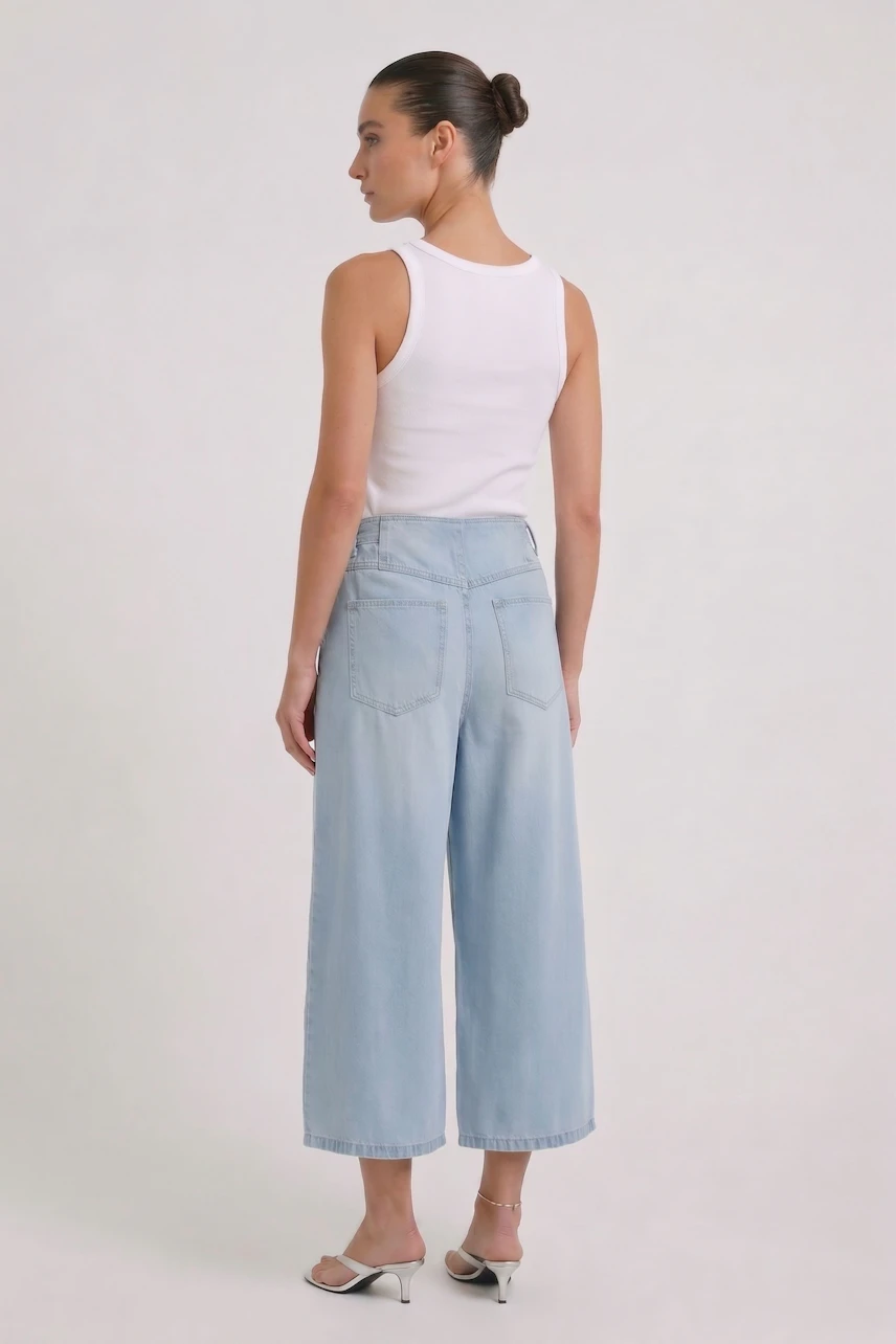Woman in light blue culottes and white tank top, viewed from the back, with hair in a bun.