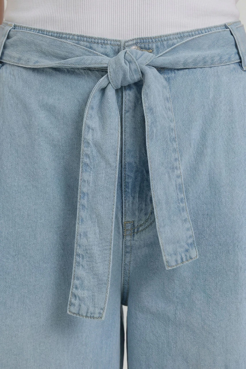 Light blue denim culotte with a tie waist, shown on a woman wearing a white top.
