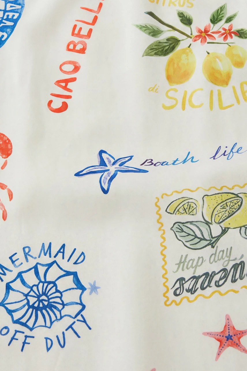 A-line dress with vibrant prints of lemons, starfish, and playful text on white fabric.