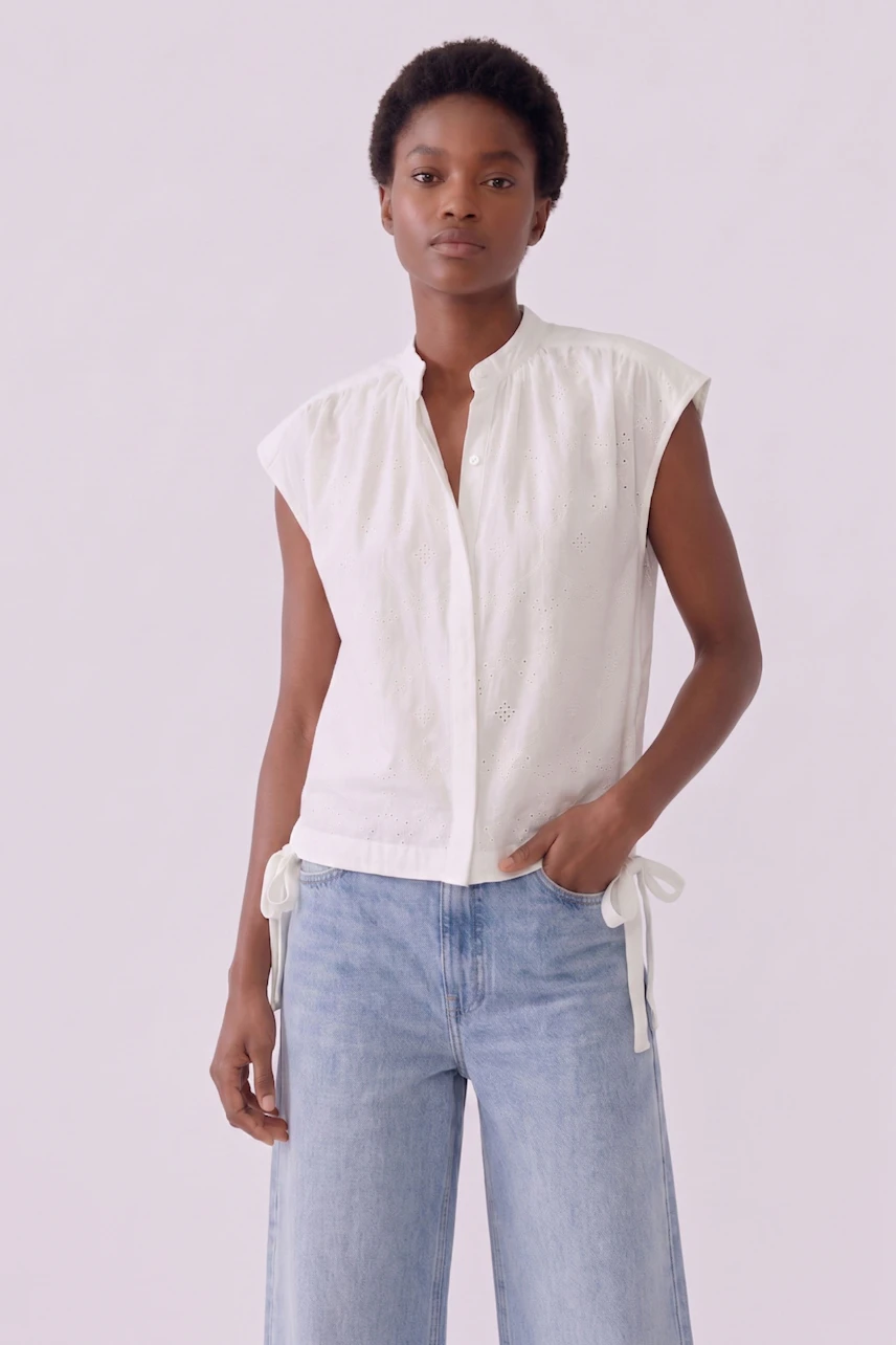 Casual blouse: Woman in a sleeveless white blouse with subtle details, paired with light blue jeans.