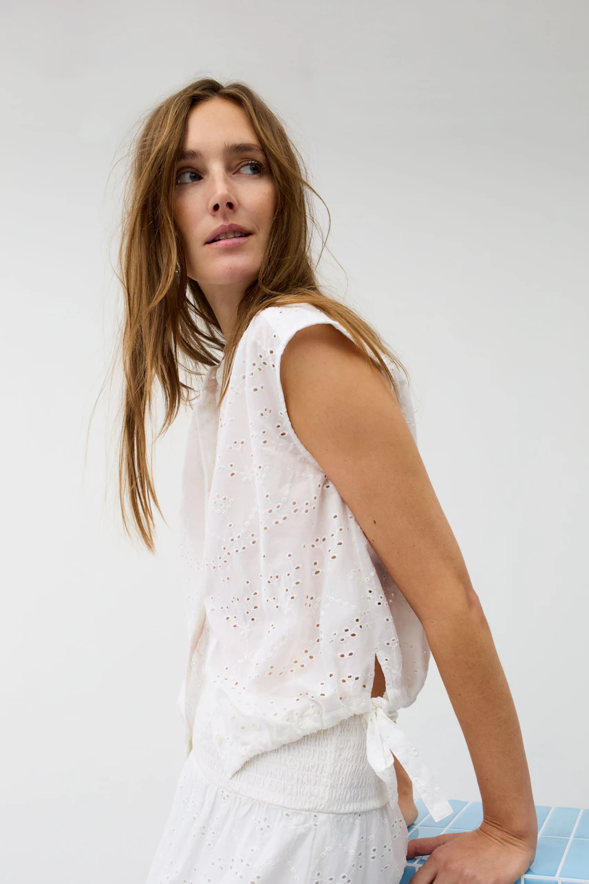 Casual blouse: Woman in a sleeveless white blouse with eyelet details, looking to the side.