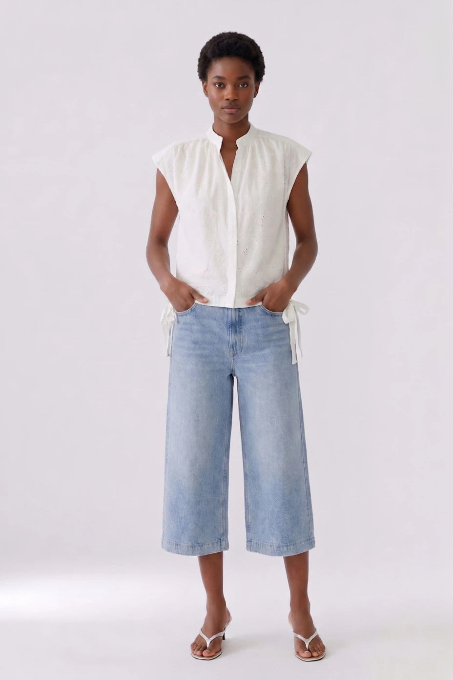 White sleeveless blouse with delicate embroidery and tie details, perfect for a casual look.