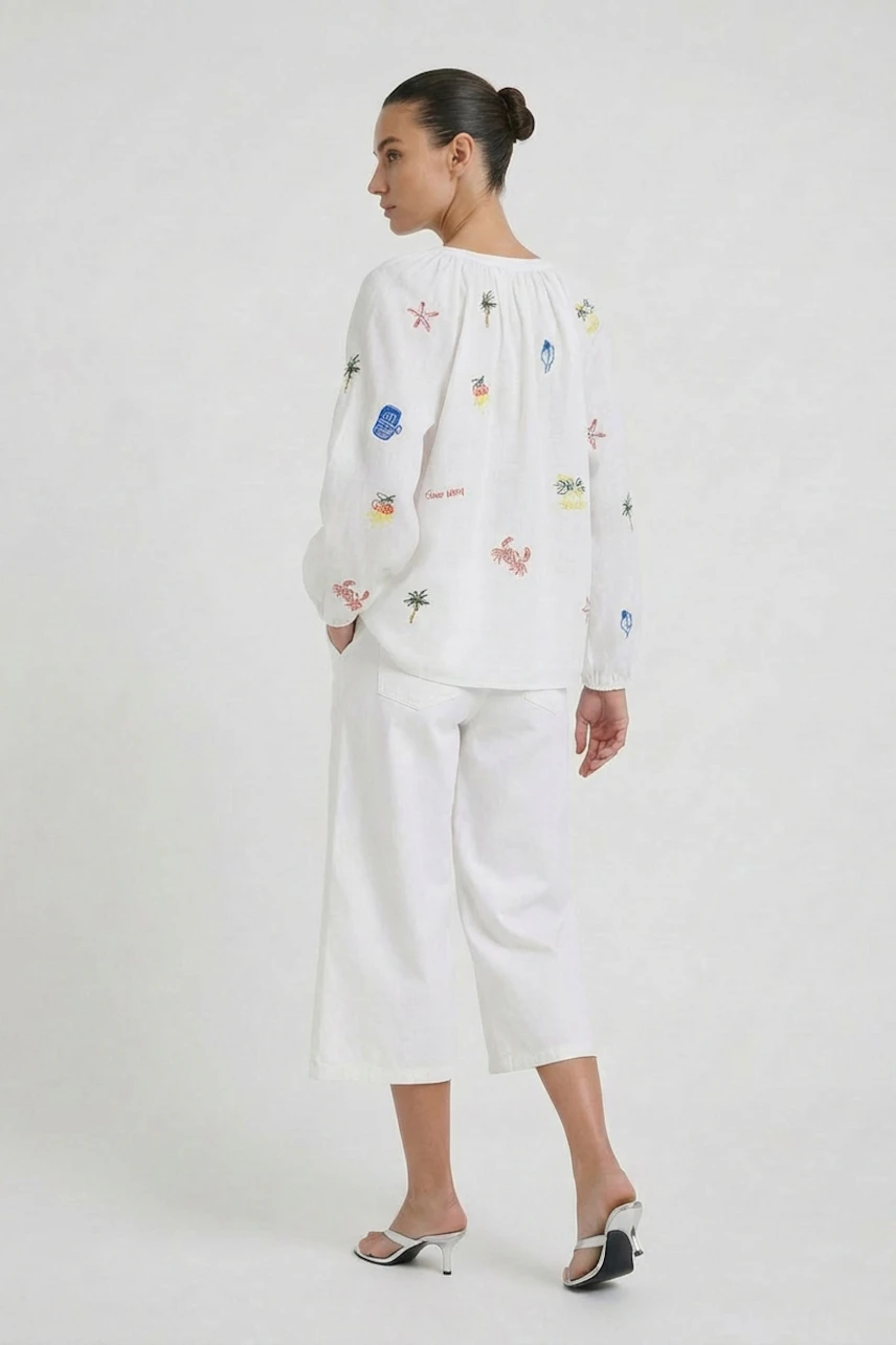 White tunic with colorful embroidery: Woman in relaxed fit, paired with white pants and heels.