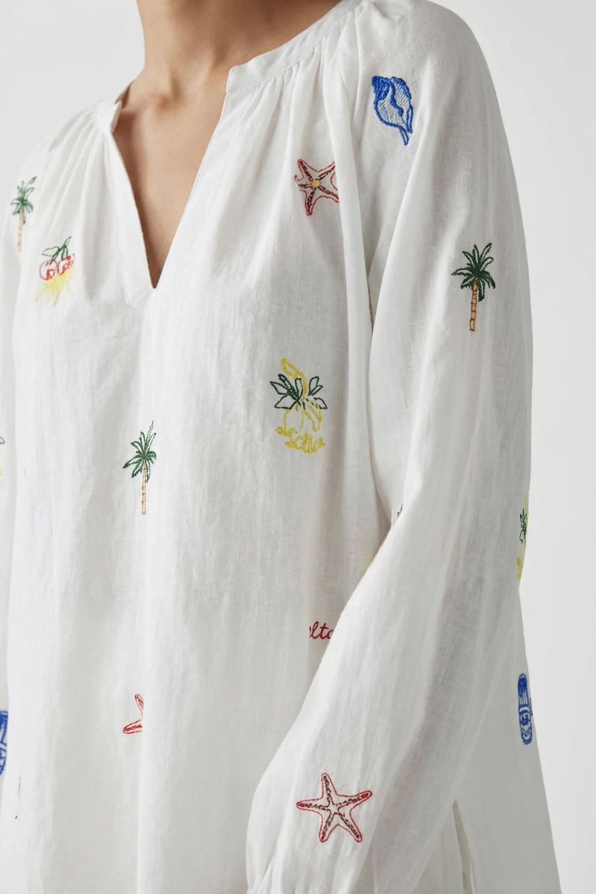 Casual tunic: Woman in a white tunic with colorful embroidery, featuring palm trees and starfish.