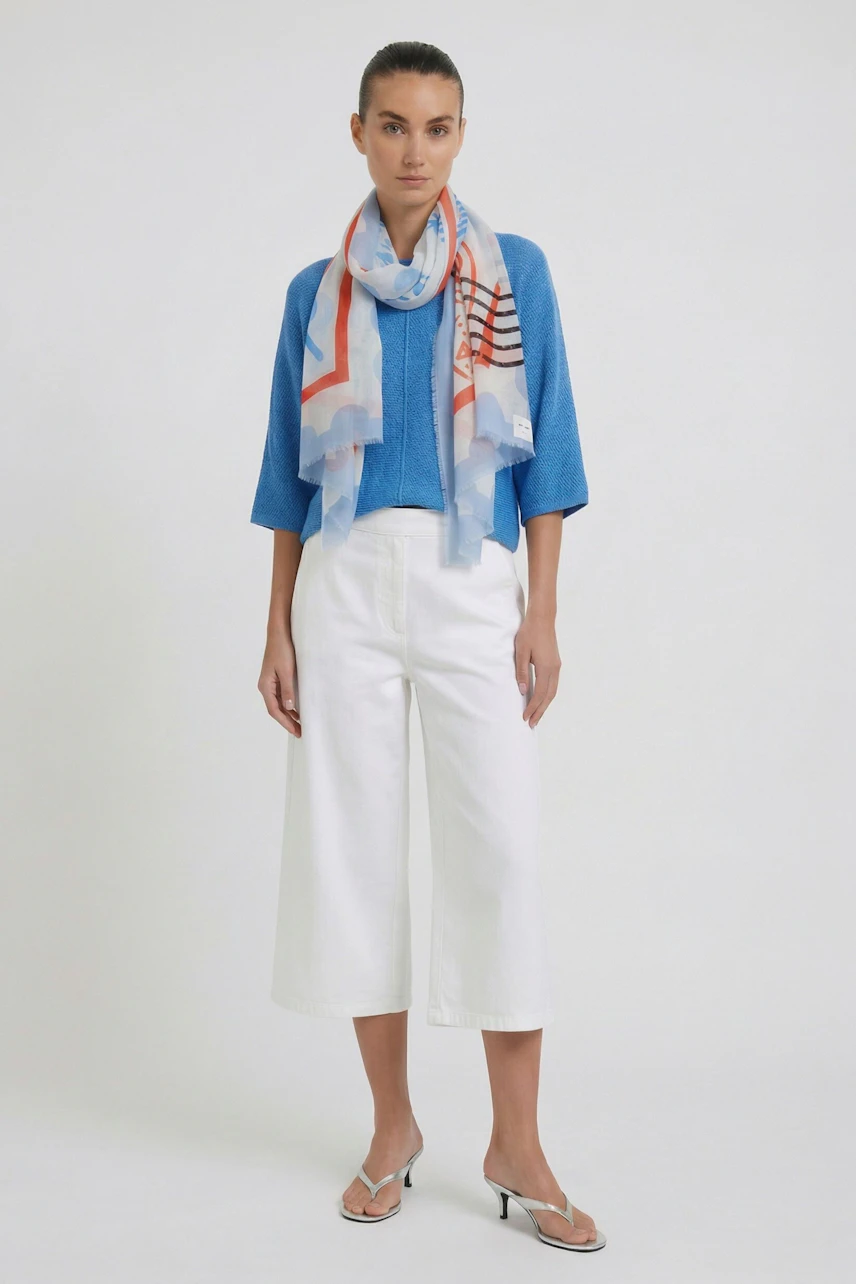 Woman in blue top and white pants wearing a colorful scarf, adding a vibrant touch to her outfit.