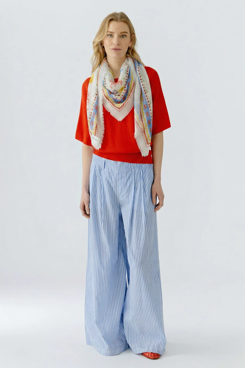 Colorful scarf on woman in red top and blue striped pants, adding a vibrant touch to the outfit.