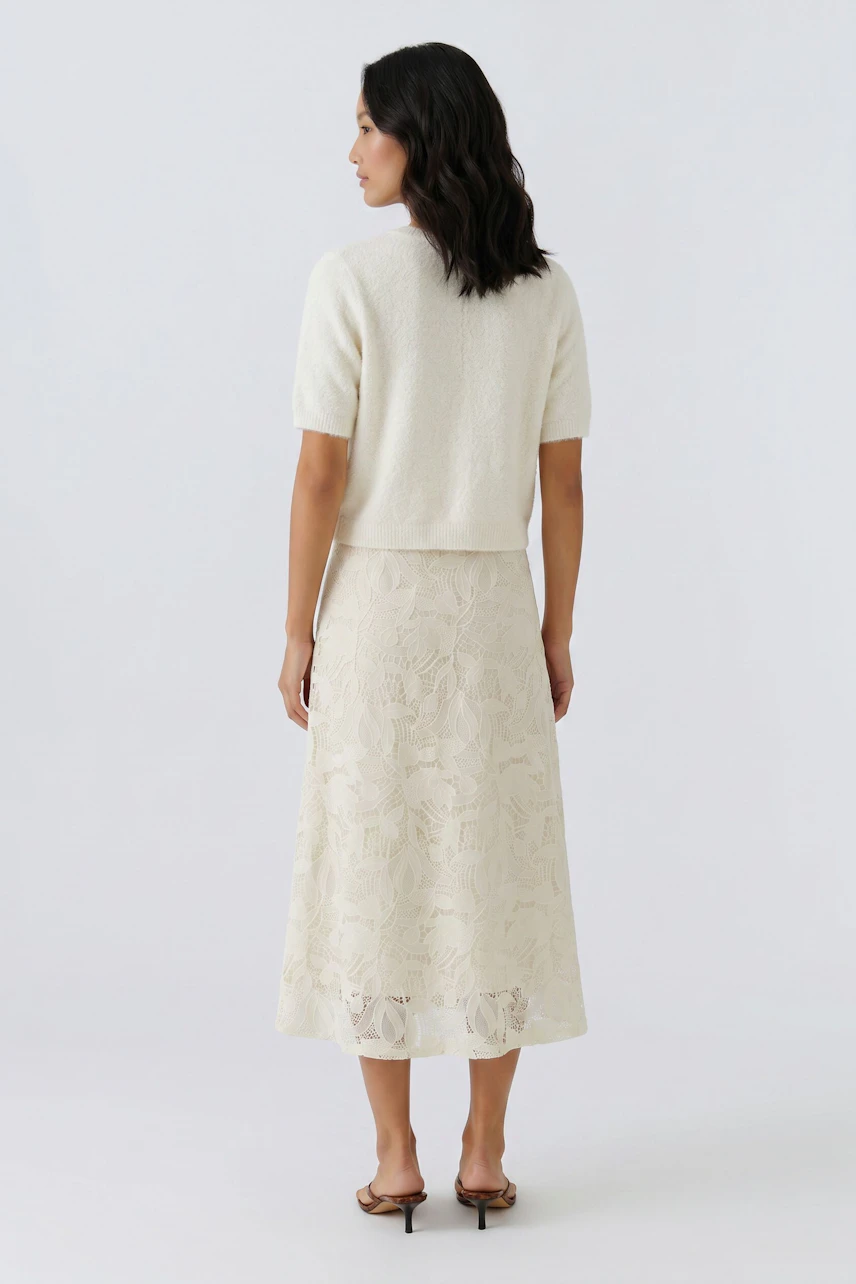 Damen A-Linien-Rock: Frau in einem hellen, floralen Rock mit Spitzen-Details und lässigem Top von hinten.