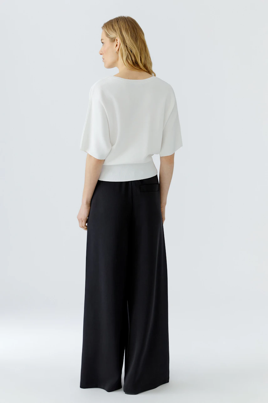 Casual women's pullover: Woman in a white pullover and black wide-leg pants, viewed from the back.