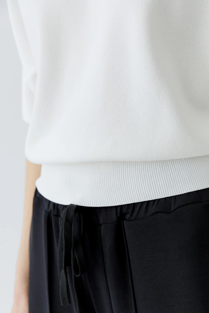 Casual white pullover: Woman in a relaxed fit, paired with black drawstring pants.