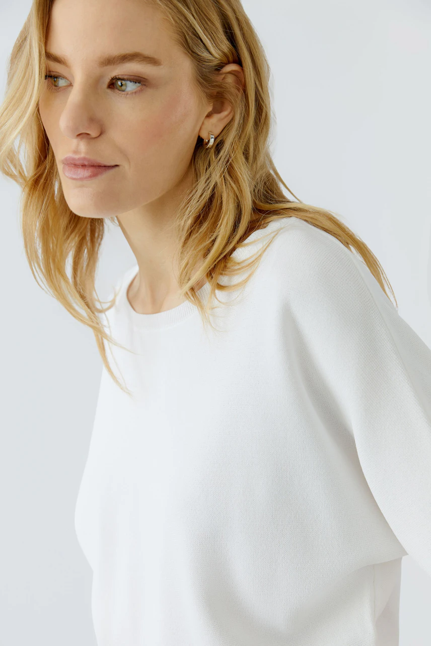 Casual women's pullover: Woman in a white pullover with a relaxed fit, looking to the side.
