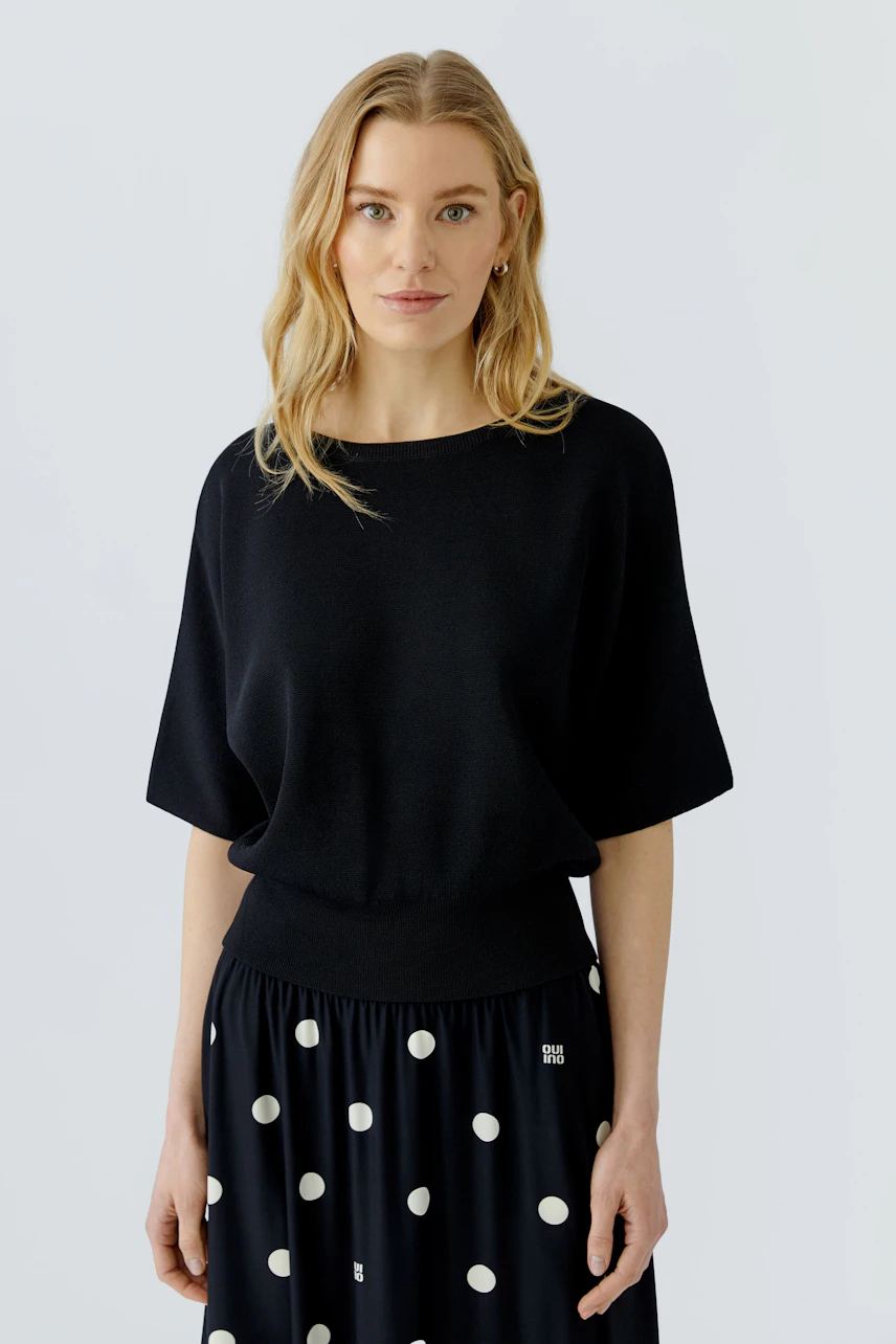 Casual women's pullover: Woman in a black pullover with wide sleeves and a polka dot skirt.